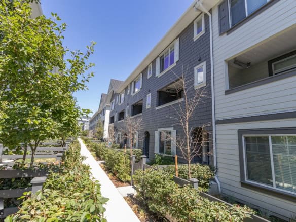 Contemporary multi-unit residential building with landscaped walkways and clear blue sky, showcasing Orca Realty Inc. expertise in Vancouver real estate.