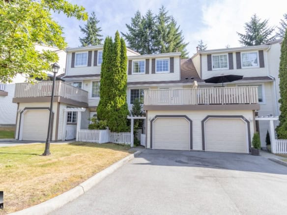 Bright multi-level townhouse with attached garages, surrounded by lush greenery and mature trees, perfect for modern living in a family-friendly community in British Columbia.