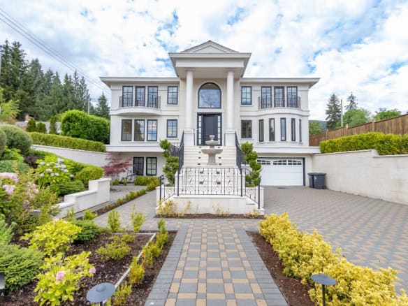 Luxurious white multi-story home with elegant columns, landscaped garden, and spacious driveway in a scenic suburban neighbourhood.