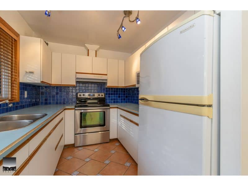 Bright kitchen with white cabinets, blue tiled backsplash, stainless steel stove, and refrigerator, perfect for modern home living in Vancouver.