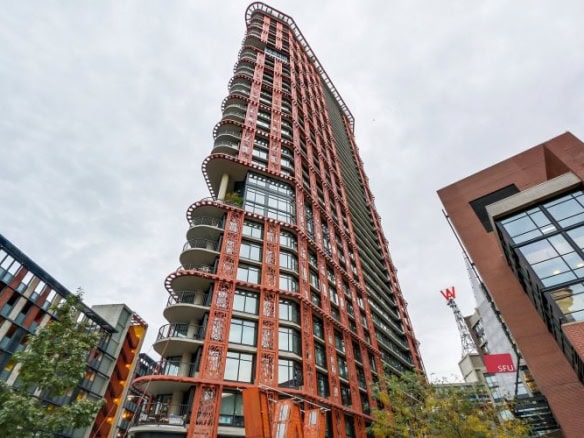 Modern high-rise residential building with distinctive orange exterior and curved balconies, located in a vibrant urban area, showcasing upscale condo living options by Orca Realty Inc.