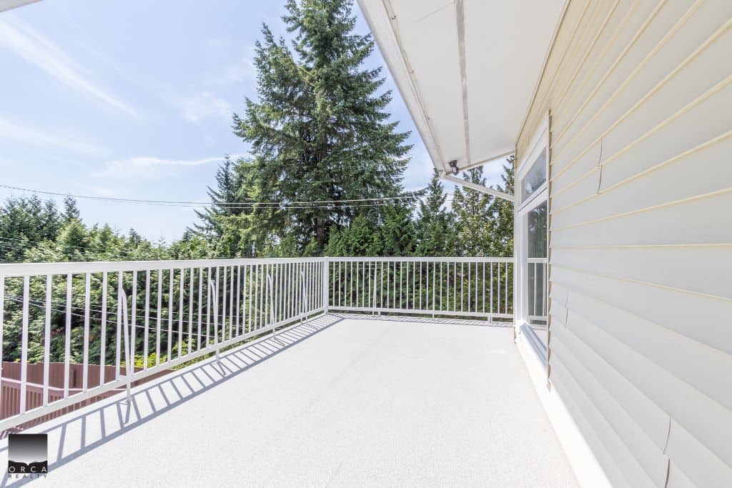 Spacious balcony with white railing and scenic views of tall evergreen trees, ideal for relaxing or entertaining, located in a residential property managed by Orca Realty Inc.