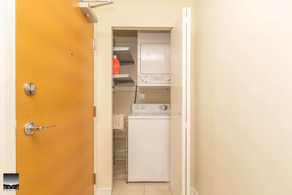 Compact laundry area with stacked washer and dryer, efficient shelving, and clean design, ideal for Vancouver homebuyers seeking functional laundry solutions.