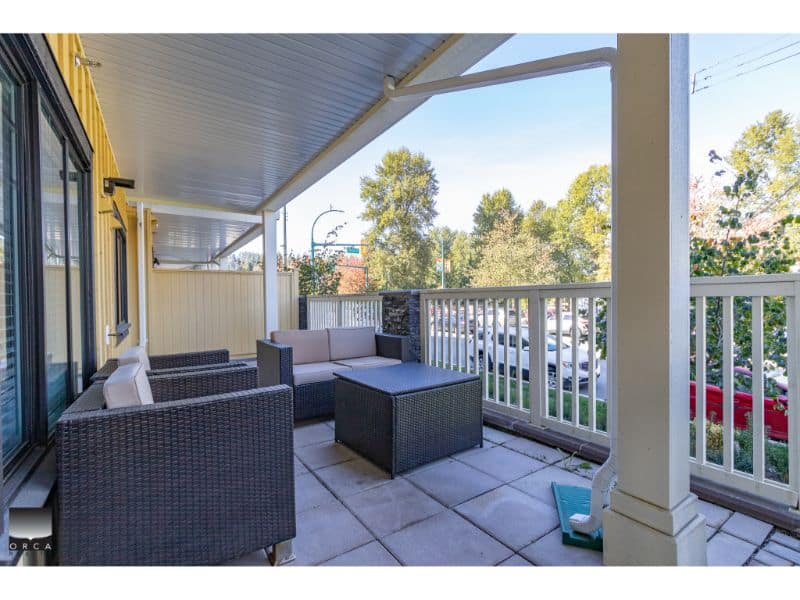 Spacious balcony with outdoor furniture including wicker sofas and a coffee table, overlooking a residential street with trees and parked cars, perfect for relaxing or entertaining.