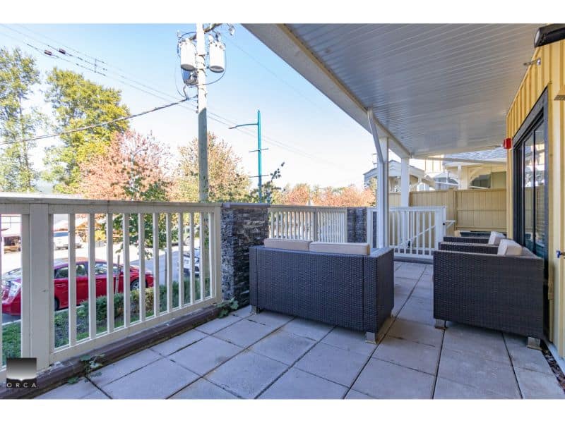 Beautiful outdoor balcony with wicker seating, overlooking a parking lot and surrounded by trees, perfect for relaxing or entertaining; part of a property listed by Orca Realty Inc.