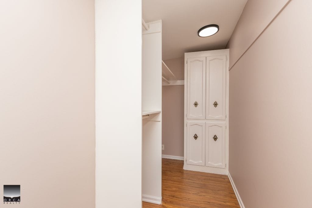 Spacious walk-in closet with white built-in storage and hardwood flooring in a modern home, showcasing efficient use of space for closet organization.