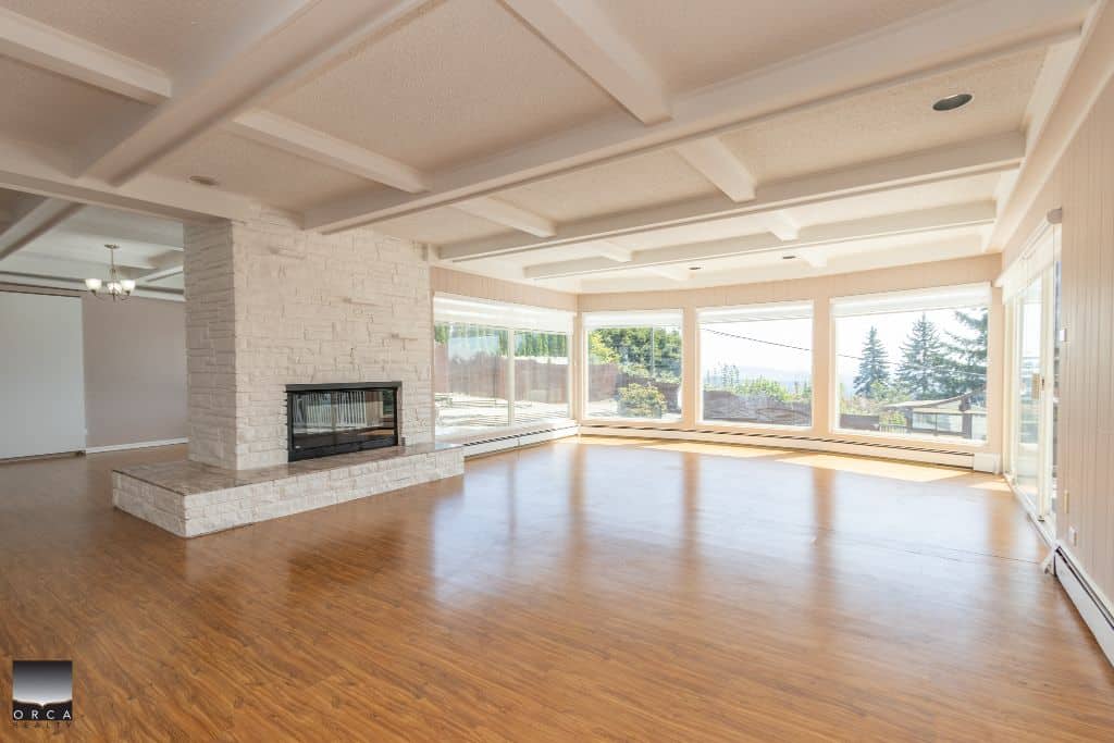 Bright living room with large windows, white brick fireplace, and hardwood flooring in a modern home listing by Orca Realty Inc.
