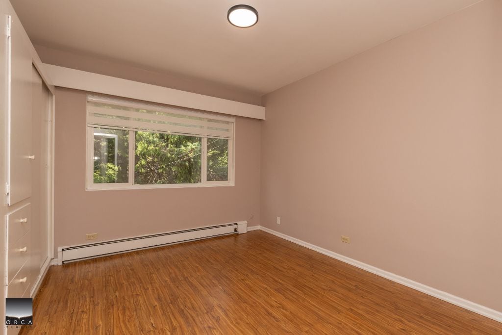 Spacious bedroom with large window, neutral wall paint, hardwood flooring, and ample natural light, ideal for Vancouver real estate buyers.
