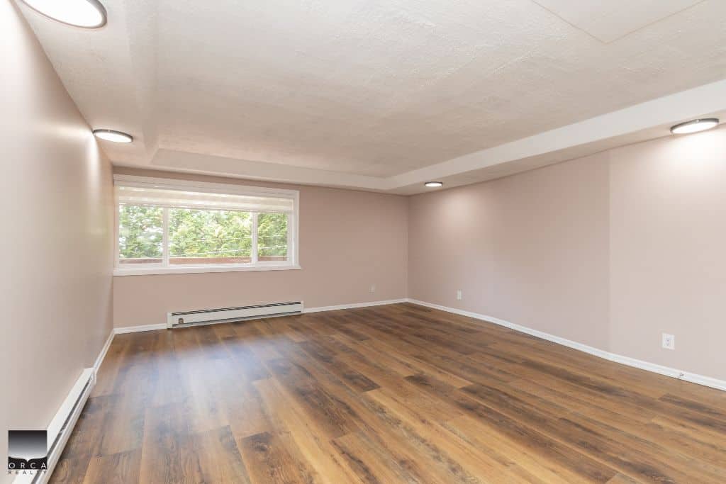 Bright spacious living room with large window, hardwood flooring, neutral walls, and recessed lighting, ideal for home buyers seeking a comfortable residential space in Vancouver.