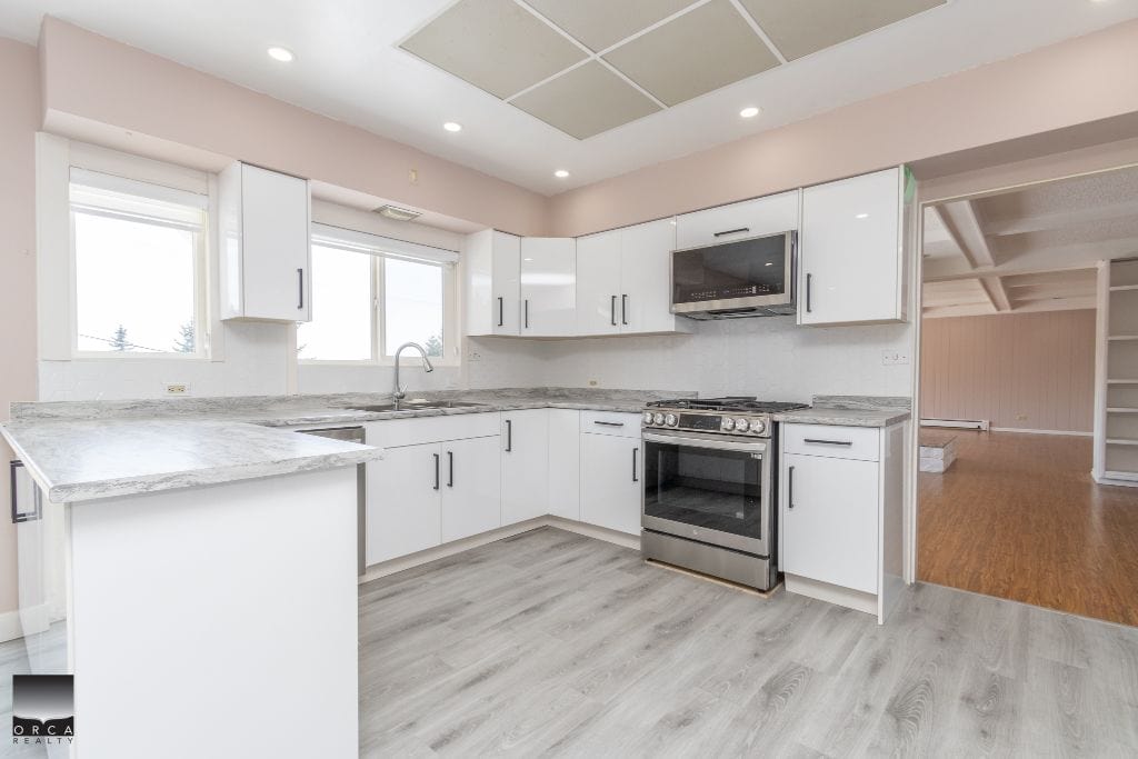 Bright modern kitchen with white cabinetry, stainless steel appliances, and granite countertops in a spacious open-concept layout. Features ample natural light from multiple windows.