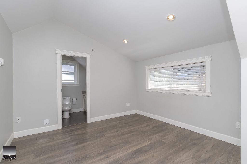 Bright modern bedroom with an en-suite bathroom, light grey walls, white trim, and laminate flooring, ideal for Vancouver Island real estate listings.