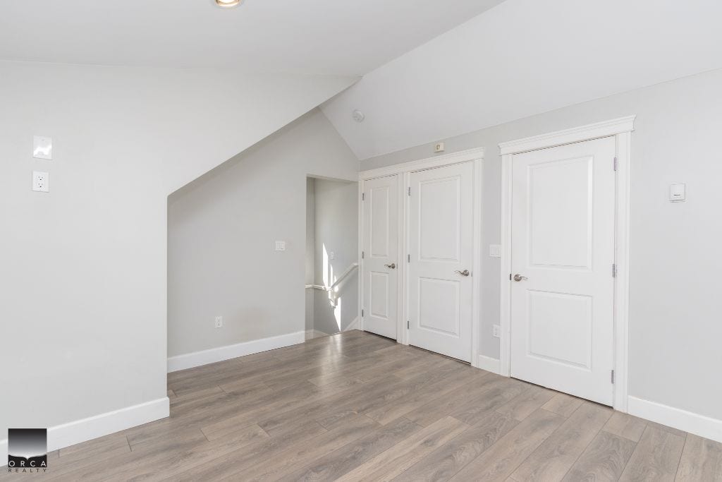 Bright and airy room with white walls, three white doors, and natural light, perfect for a modern Vancouver home or condo. Hardwood flooring adds warmth to this spacious interior.