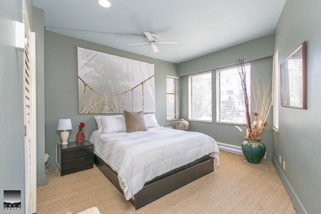 Cozy bedroom with large windows, modern decor, and calming green walls for a comfortable living space. Perfect for homeowners and real estate buyers seeking a serene home environment.