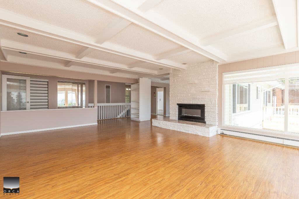 Spacious living room with hardwood floors, modern fireplace, large windows, and bright natural light in a beautiful home listed by Orca Realty Inc.