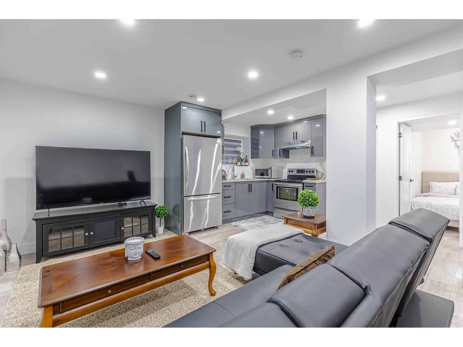 Bright modern living room with open-concept kitchen, featuring stainless steel appliances, grey cabinetry, and contemporary furnishings, ideal for Vancouver Island real estate and property investments.