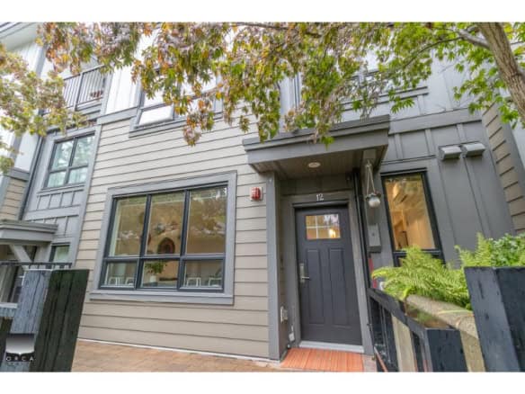 Contemporary grey townhouse exterior with modern black door, surrounded by lush greenery and trees, featuring large windows, ideal for Vancouver real estate listings and property sales.