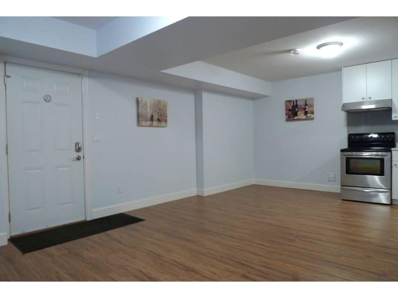 Spacious modern basement apartment with hardwood flooring, white walls, and stainless steel kitchen appliances, ideal for comfortable living in a peaceful neighbourhood.