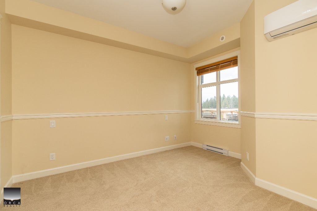Spacious beige bedroom with large window, wall-mounted air conditioner, and neutral carpeting, ideal for Vancouver Island homebuyers seeking comfortable real estate options.