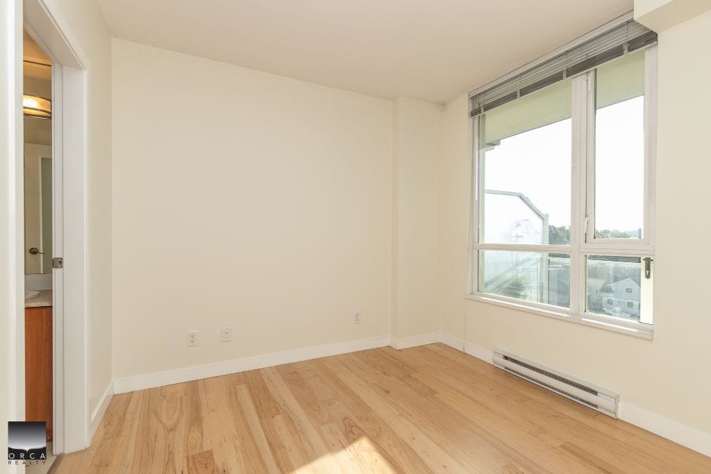 Bright empty bedroom with large window and hardwood flooring at Orca Realty Inc. showcasing modern rental or sales listing options in Vancouver.