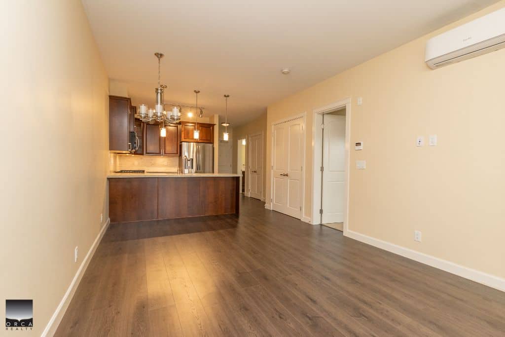 Spacious open-concept living area with modern kitchen, dark wood flooring, and neutral walls, ideal for Vancouver Island real estate buyers.