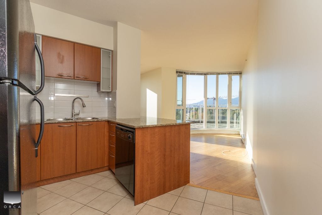 Modern kitchen with wooden cabinets and stainless steel appliances in an Ottawa apartment for sale or rent. Bright living space with large windows and scenic mountain views, perfect for urban living.