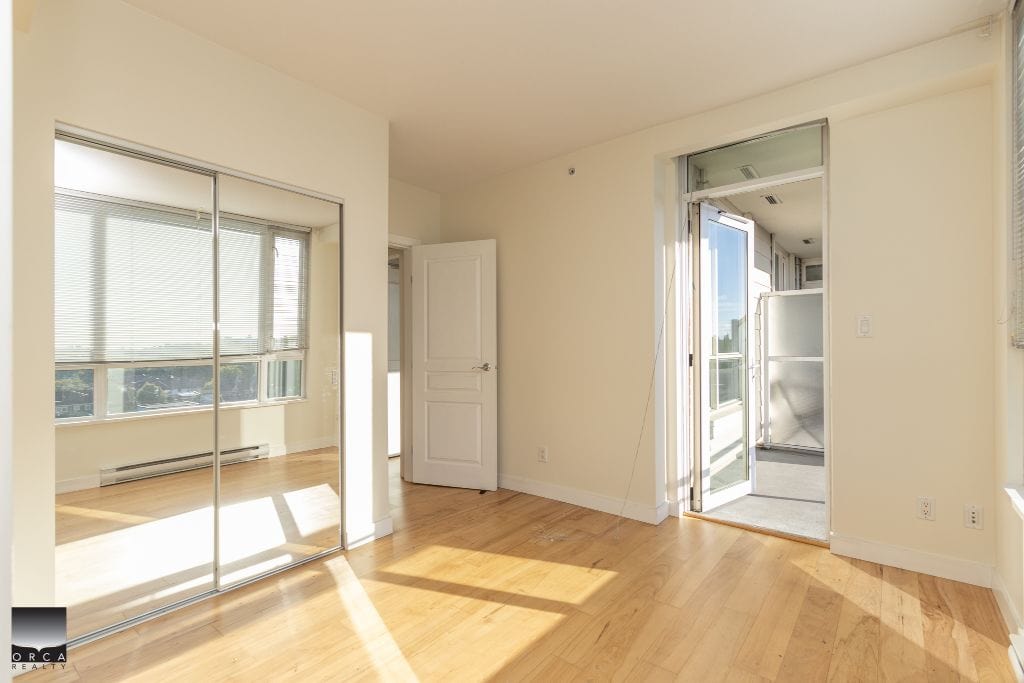 Bright and airy bedroom with large windows, hardwood flooring, and a closet with mirrored sliding doors, showcasing a modern interior ideal for condo living in Vancouver.