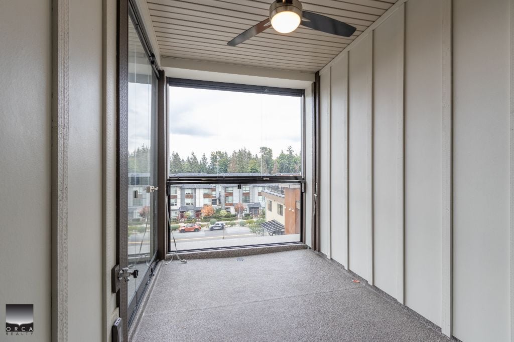Bright enclosed balcony with large windows, overlooking a residential neighborhood and green trees, ideal for relaxing or outdoor entertainment in a condo unit.