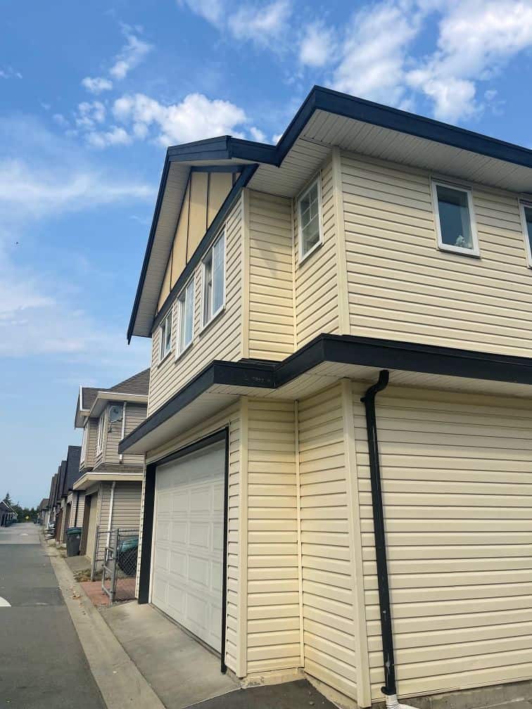 Modern multi-family residential home with beige siding and a garage, located in a quiet neighborhood under a bright blue sky.