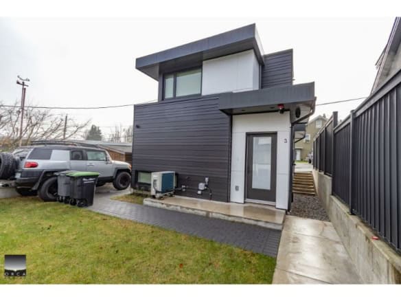 Contemporary modern duplex home with sleek black and white exterior, situated in a residential neighbourhood with a grassy yard, driveway, and privacy fencing, perfect for real estate investment or living.