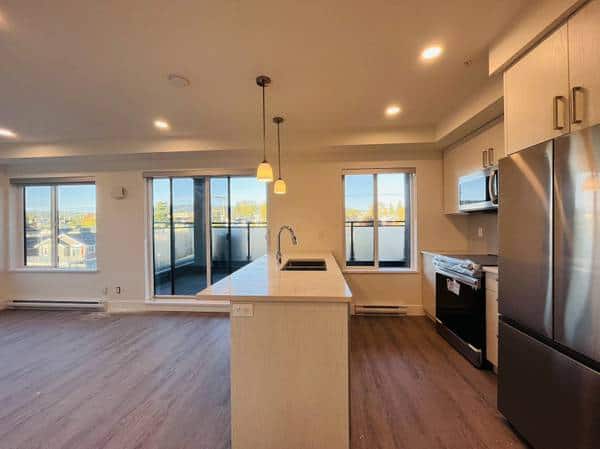 Spacious modern kitchen with stainless steel appliances, white cabinetry, large windows, and open-plan living area in a Vancouver real estate listing.