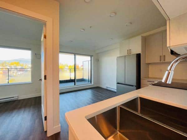 Modern open-plan kitchen and living room with large windows and natural light in a Vancouver real estate listing.
