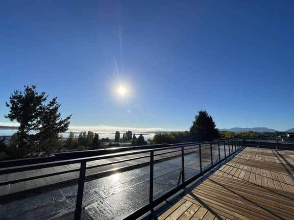 Sunlit oceanview balcony with wooden decking and metal railing, showcasing a serene waterfront scene perfect for real estate listings and property marketing in Vancouver Island.