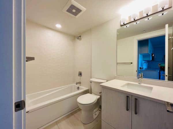 Modern bathroom with bathtub, toilet, and vanity featuring a large mirror and contemporary lighting for Vancouver real estate listings.