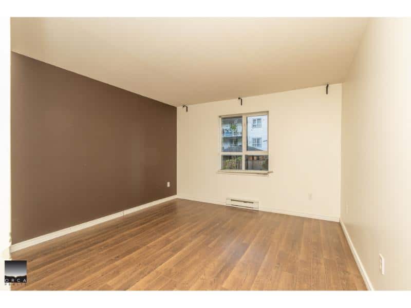 Modern empty living room with hardwood floors and white walls, ideal for Vancouver real estate. Featuring a large window, neutral decor, and ample space for customization.