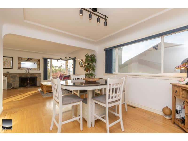 Bright dining area with white furniture and hardwood flooring, open living space with large windows, cozy fireplace, and stylish decor in a Vancouver home.