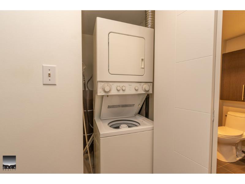 Stacked washer and dryer unit in a modern laundry room, conveniently located near the bathroom, with neutral decor and efficient space utilization.
