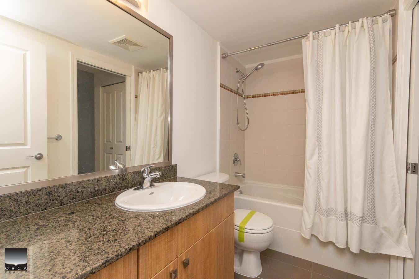 Bright modern bathroom with a granite countertop, oval sink, and a shower/tub combo with white curtain, ideal for Vancouver property listings.