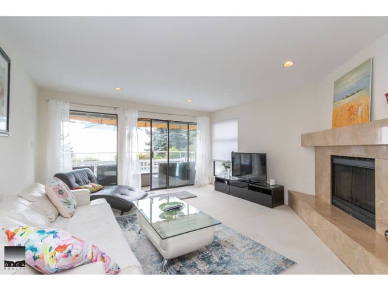 Bright living room with large sliding glass doors leading to balcony, modern furniture, and fireplace, showcasing a comfortable and stylish interior by Orca Realty Inc.