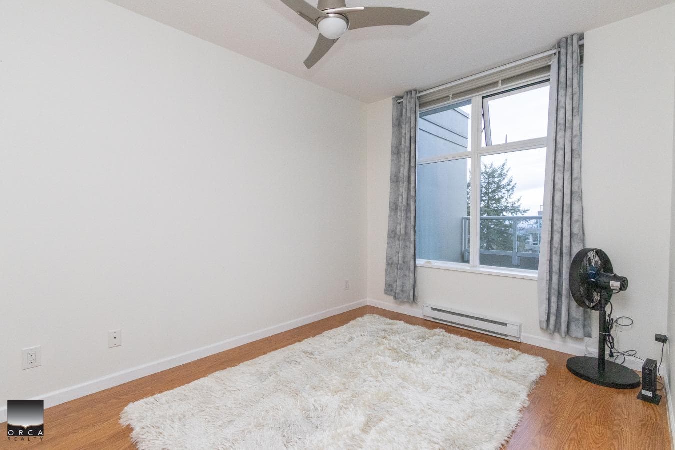 Bright minimalist bedroom with large window, light carpeting, modern ceiling fan, and neutral decor, perfect for Vancouver or Victoria property buyers seeking contemporary rental or living space.