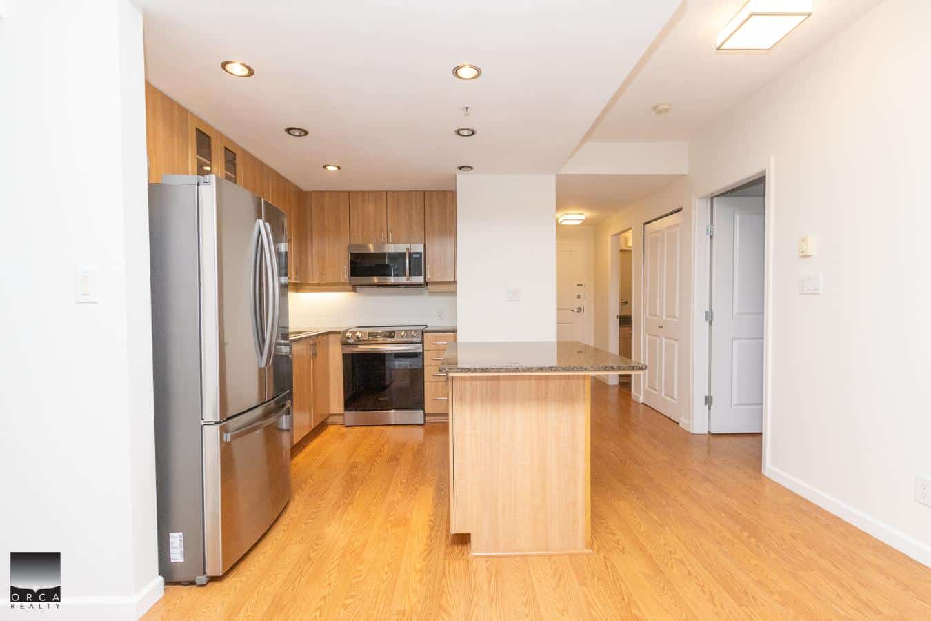 Modern kitchen with stainless steel appliances, wooden cabinetry, granite countertops, and hardwood flooring in a contemporary Orca Realty listing.