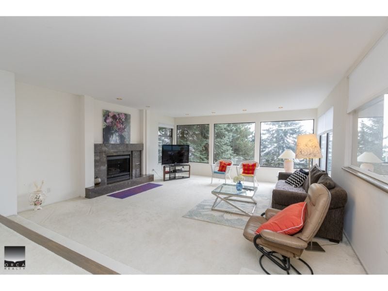 Bright living room with large windows overlooking lush greenery, modern fireplace, and cozy seating area, perfect for relaxed living and showcasing Vancouver real estate.