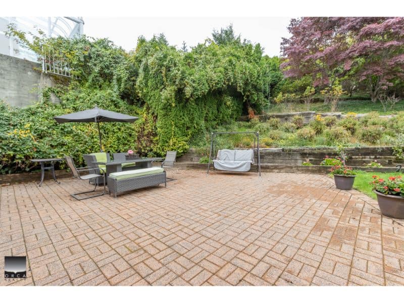 Bright outdoor patio with garden furniture, umbrella, and potted plants, perfect for relaxing and entertaining amidst lush greenery and terraced landscaping in Victoria, BC.