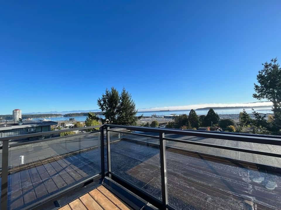 Breathtaking waterfront view from a balcony in Vancouver, BC, featuring a clear blue sky, lush trees, and a scenic water landscape, perfect for real estate listings and property showcase.