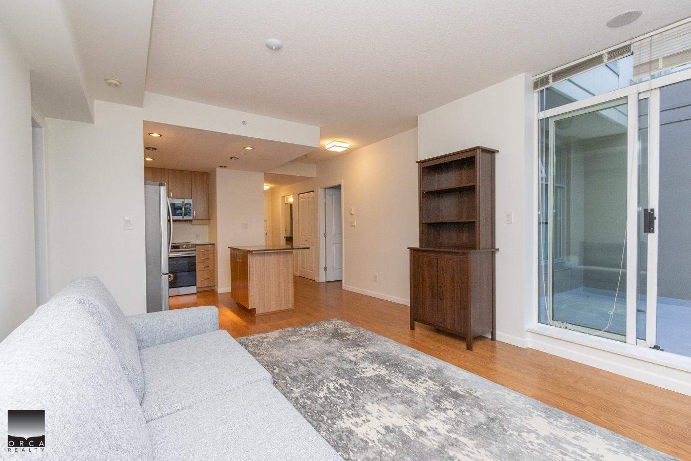 Modern open-concept living room with large windows, hardwood floors, and stylish furniture, located in a Vancouver condo listed by Orca Realty Inc., offering prime real estate in BC.