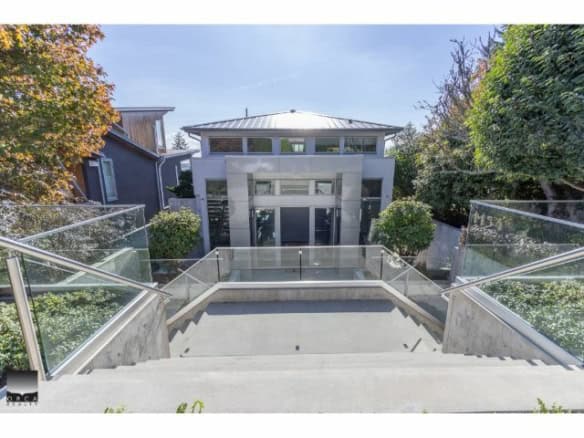 Stunning modern house with glass railings and landscaped greenery, showcasing contemporary architecture perfect for upscale real estate listings.
