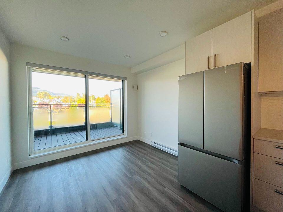 Bright condo interior with sliding glass door leading to balcony, modern kitchen appliances, ideal for Vancouver real estate buyers, showing spacious and contemporary living space.