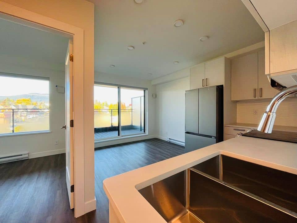 Modern Vancouver Island condo with open-plan kitchen and living area, large windows, and balcony access, perfect for waterfront living in Orca Realty Inc. listings.