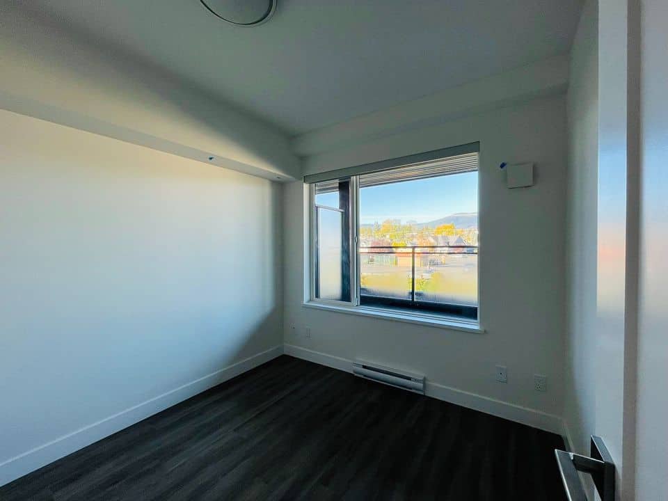 Bright empty modern bedroom with large window showcasing city views, white walls, dark flooring, and natural light from outside. Perfect for homebuyers seeking contemporary condos or apartments in BC.