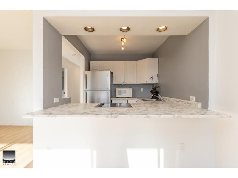 Modern kitchen with white cabinetry, stainless steel appliances, and a marble breakfast bar, perfect for Vancouver Island real estate buyers.