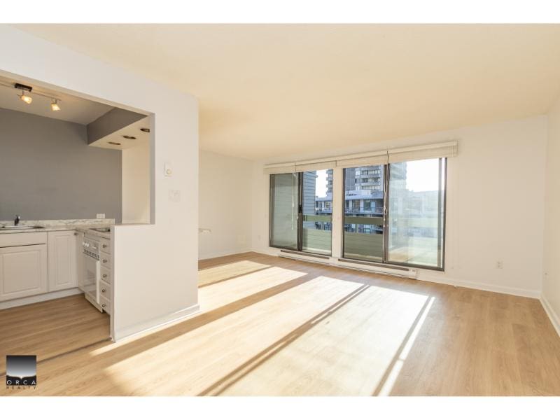 Bright, sunlit living room with large windows and hardwood floors in a modern apartment, showcasing contemporary design and urban views available through Orca Realty Inc.